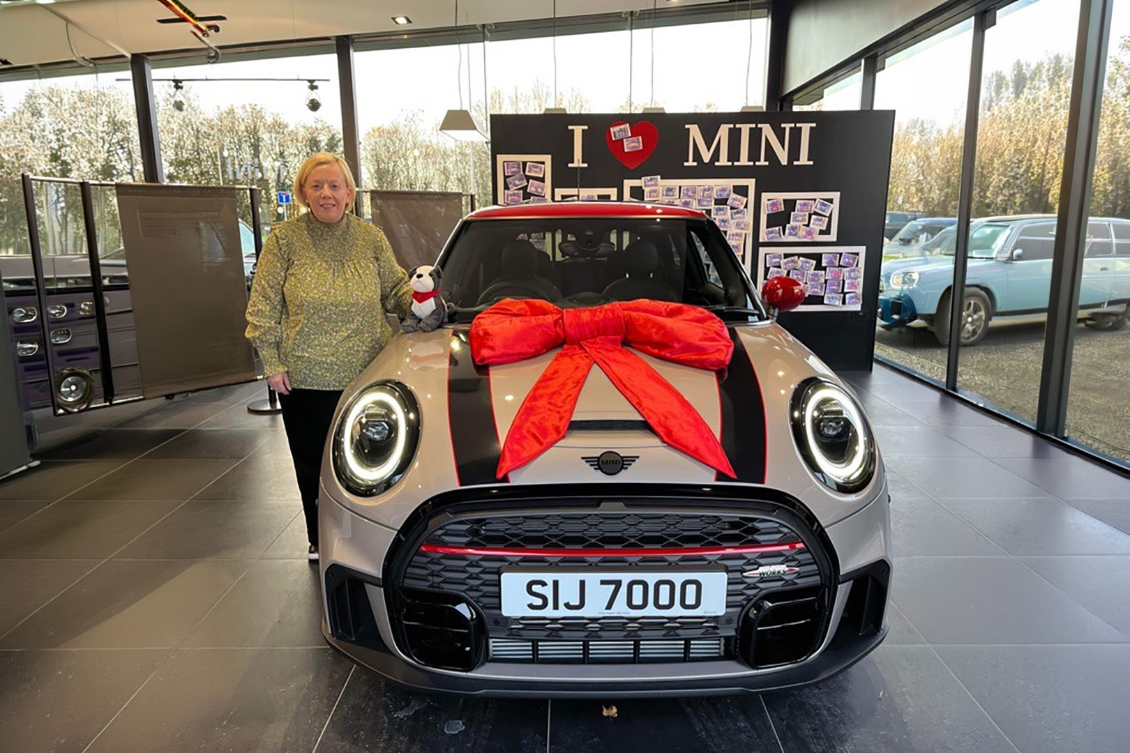 MINI car displayed indoors in a showroom with a large red gift bow on the bonnet